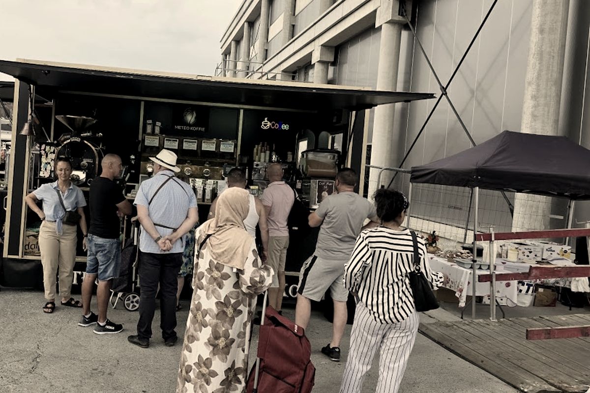 Standul Meteo Koffie la Marché de l'Abattoir, cu oameni așteptând la tejghea.